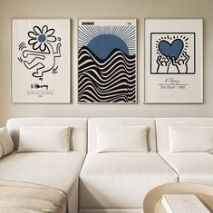 three paintings hang on the wall above a white couch