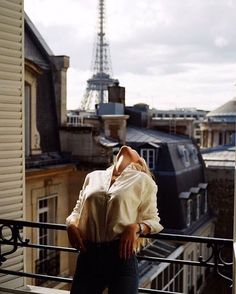 a woman standing on top of a balcony next to a building with the eiffel tower in the background