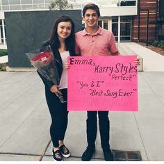 a man and woman standing next to each other holding a pink sign with writing on it