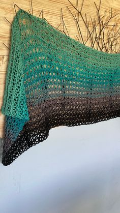 a crocheted green and black blanket hanging on a wooden wall