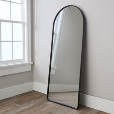 a large black mirror sitting on top of a wooden floor next to a white wall