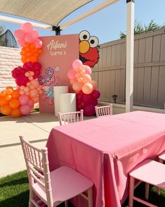 a pink table and chairs with balloons on the wall behind it, along with an elmo sesame street sign