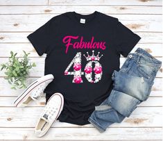 a black shirt with pink flowers and the words sweet 20th birthday on it next to some jeans