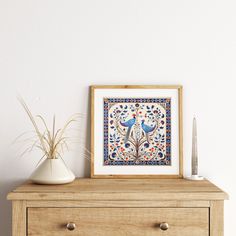 a white vase sitting on top of a wooden dresser next to a framed artwork piece