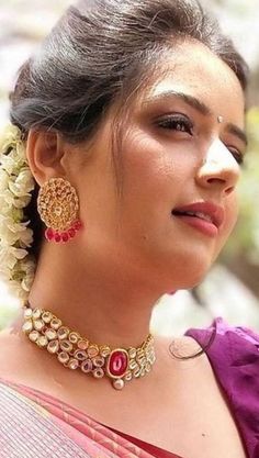 a woman wearing a necklace and earrings with flowers in her hair, looking off to the side