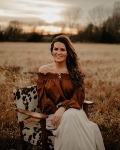 a woman sitting on a chair in the middle of a field smiling at the camera