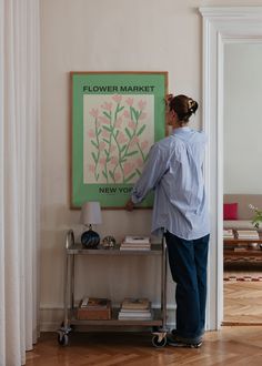 a woman standing in front of a flower market poster on a wall next to a table