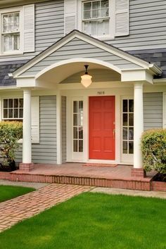 a red door is on the front of a gray house with white trim and brick steps