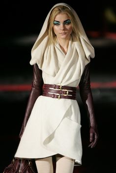 a woman in white dress and black gloves walking down a runway with her hand on her hip