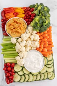 a platter filled with vegetables and dips on top of each other, including cauliflower, carrots, celery, cucumber, broccoli