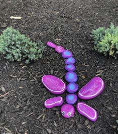 a purple and blue sculpture sitting on top of a dirt field next to green bushes