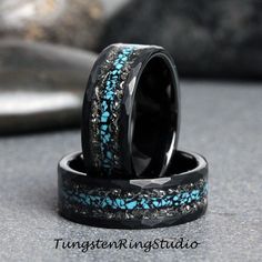 two wedding bands with blue and black stones inlayed to them, sitting on top of each other