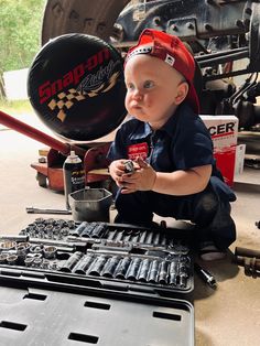 a baby sitting on the ground next to an open toolbox and wrenches in his hands