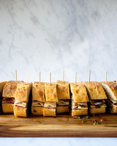 a wooden cutting board topped with sandwiches on top of each other and toothpicks sticking out of them