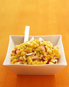 a white bowl filled with corn salad on top of a wooden table next to a fork