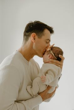 a man holding a baby in his arms and kissing it's face with the other hand