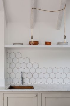 a kitchen with white hexagonal tiles and wooden cabinets, along with an open shelf above the sink