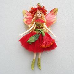 a red and green fairy doll hanging on the wall with her hands in her pockets