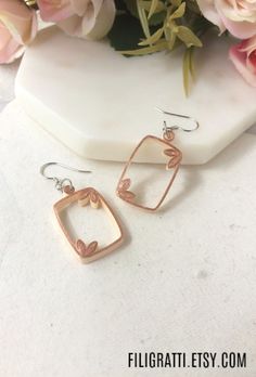 two pairs of earrings sitting on top of a white table next to flowers and a vase with pink roses