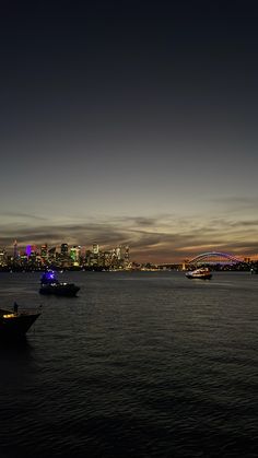 two boats floating on top of a large body of water near a city at night