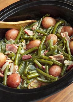 a crock pot filled with green beans, potatoes and ham on top of a wooden table