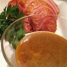 a plate with ham and parsley on it next to a glass bowl filled with gravy