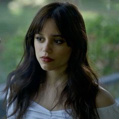 a woman with long dark hair wearing a white shirt and looking off into the distance