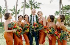 a group of women standing next to each other in front of palm trees and flowers