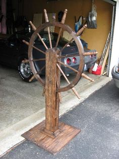 an old wooden spinning wheel in front of a garage with two cars parked behind it