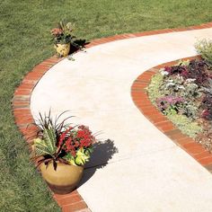 a large planter filled with lots of flowers on top of a brick walkway next to a lush green field