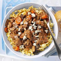 a white bowl filled with pasta and meat on top of a blue tray next to bread