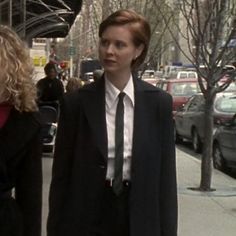 a woman in a suit and tie walking down the street with another woman behind her