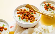 three small bowls filled with food on top of a yellow table cloth and wooden spoons