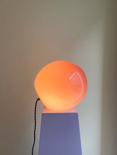 an orange lamp sitting on top of a purple table next to a white wall and floor