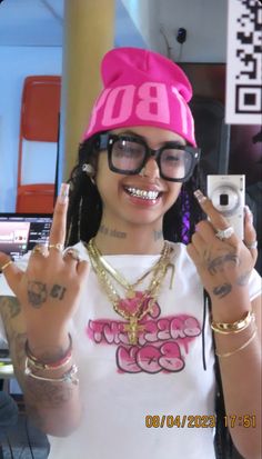 a woman with glasses and a pink hat holding up two fingers