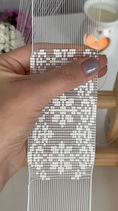 a woman's hand holding up a piece of white fabric next to a weaving machine