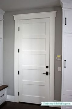 a white door in the corner of a room next to a bench and cabinet with drawers