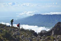 two hikers on the top of a mountain with low clouds in the valley below