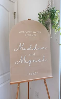 a welcome sign for the couple to be married in front of a door with a potted plant