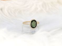 a green ring sitting on top of a white cloth covered table next to a feather