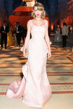 a woman in a pink dress walking down a hall with other people standing around her