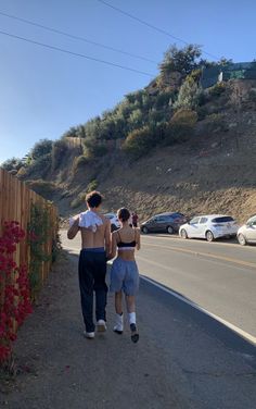 two people walking down the street in front of a fence