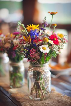 two mason jars filled with colorful wildflowers on top of a burlap table cloth