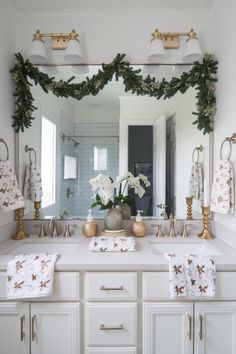 a white bathroom with gold accents and flowers on the counter top, surrounded by greenery