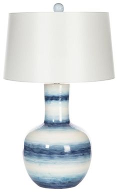 a blue and white vase with a white shade on it's side, sitting next to a lamp