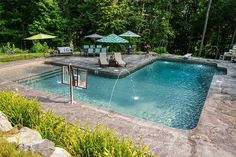 an empty swimming pool surrounded by trees and lawn chairs with umbrellas in the background