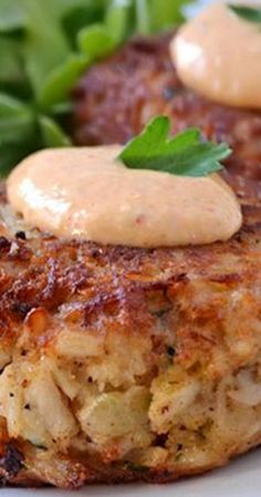 two crab cakes on a white plate with some greens and sauce in the middle, ready to be eaten