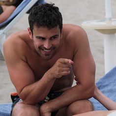 a shirtless man sitting next to a woman on a towel at the beach with his hand in her pocket