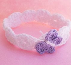 two crocheted hearts are attached to a white and purple bracelet on a pink background