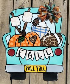 a blue truck with pumpkins and other items in the back is hanging on a wooden fence